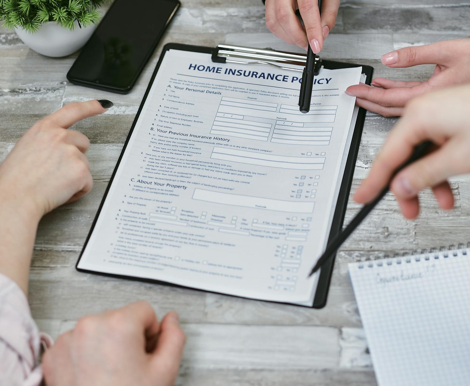 pexels-photo-7731335 - Eric Felt Insurance Three individuals collaborating on a home insurance policy document. Elements include a clipboard, notes, and pointing hands.