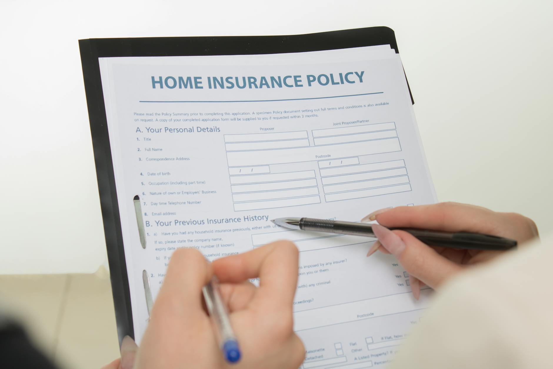 pexels-photo-7736032 - Eric Felt Insurance Hands holding pens filling out a home insurance policy document for coverage details.