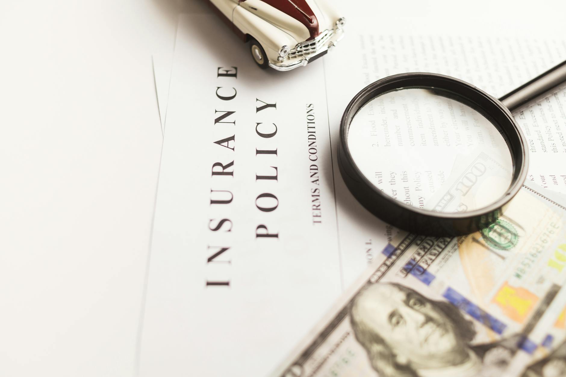 pexels-photo-10341357 - Eric Felt Insurance Close-up image of an insurance policy with a magnifying glass, money, and toy car.